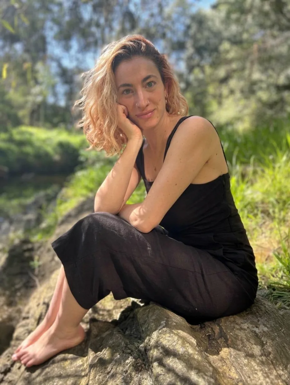 Renee Bones sitting on a rock beside a creek in bushland.